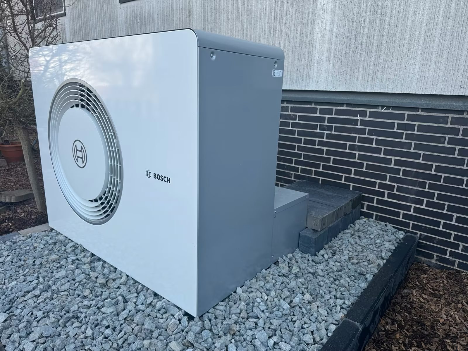 Außeneinheit einer Wärmepumpe auf Kiesbett vor einer Hauswand